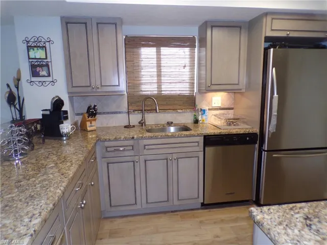 Kitchen featuring appliances with stainless steel finishes, light stone countertops, backsplash, light wood finished floors, and gray cabinetry