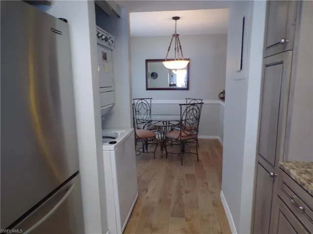 Kitchen with freestanding refrigerator, stacked washing machine and dryer, light wood finished floors, and decorative light fixtures