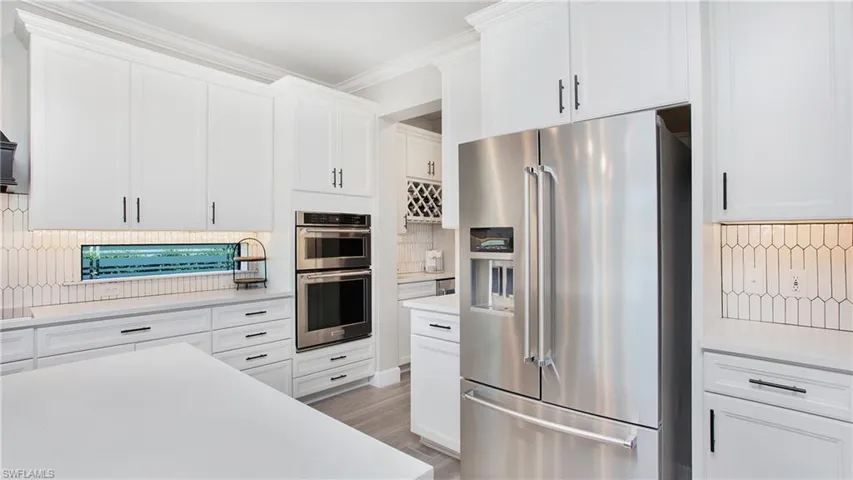 Kitchen with appliances with stainless steel finishes, backsplash, white cabinetry, and crown molding