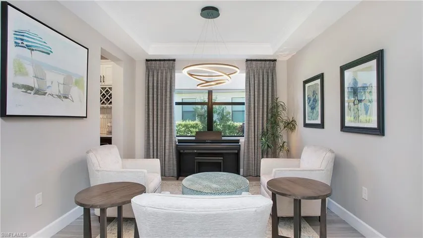 Living area with hardwood / wood-style flooring, a notable chandelier, a raised ceiling, and ornamental molding