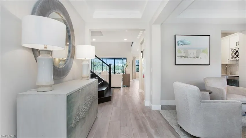 Hallway featuring a tray ceiling, beverage cooler, crown molding, sink, and light hardwood / wood-style flooring