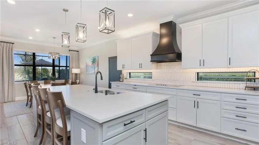Kitchen featuring pendant lighting, custom exhaust hood, a center island with sink, white cabinets, and sink