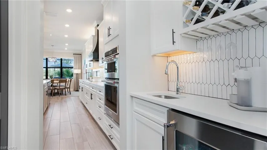 Kitchen with crown molding, sink, wine cooler, white cabinetry, and stainless steel double oven