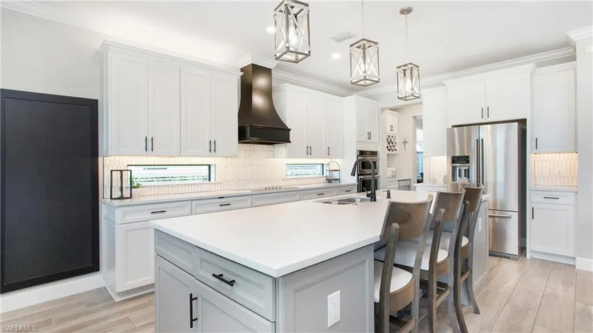 Kitchen featuring hanging light fixtures, stainless steel appliances, a kitchen island with sink, white cabinets, and custom exhaust hood