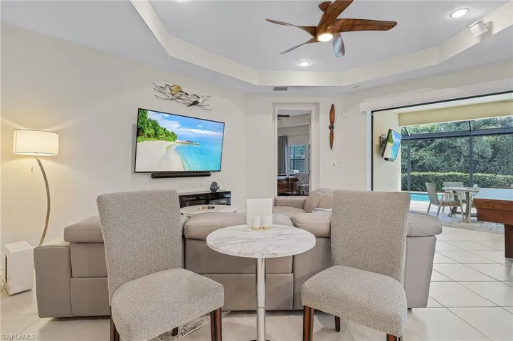 Living room featuring a tray ceiling, ceiling fan, and light tile floors