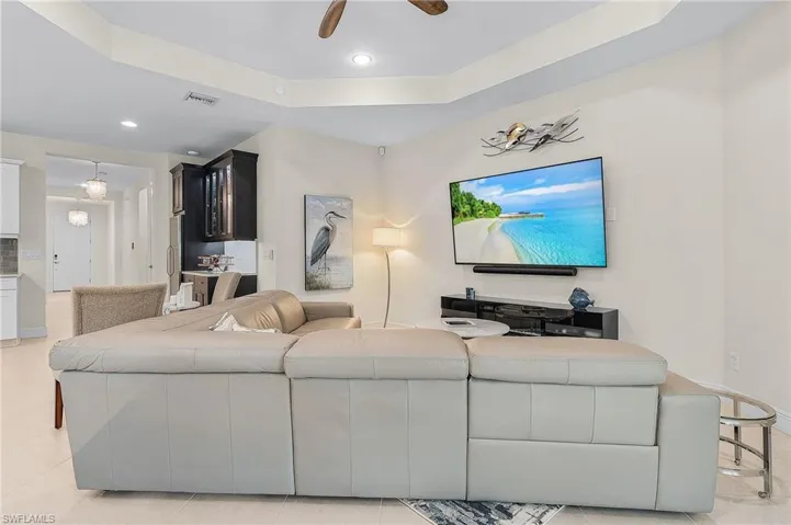 Living room featuring a tray ceiling, ceiling fan, and light tile floors