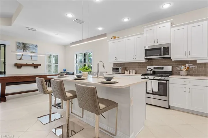 Kitchen with a center island with sink, pendant lighting, light tile floors, white cabinets, and appliances with stainless steel finishes