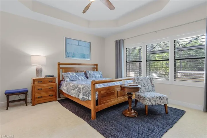 Carpeted bedroom with ceiling fan, multiple windows, and a tray ceiling