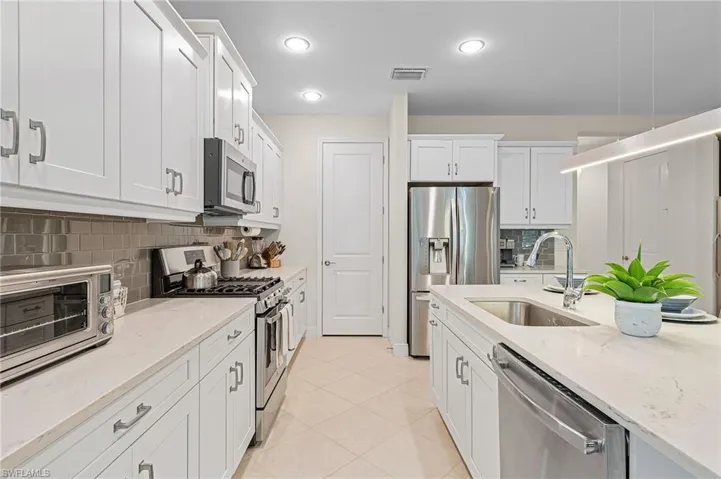Kitchen with backsplash, light tile floors, sink, white cabinets, and appliances with stainless steel finishes