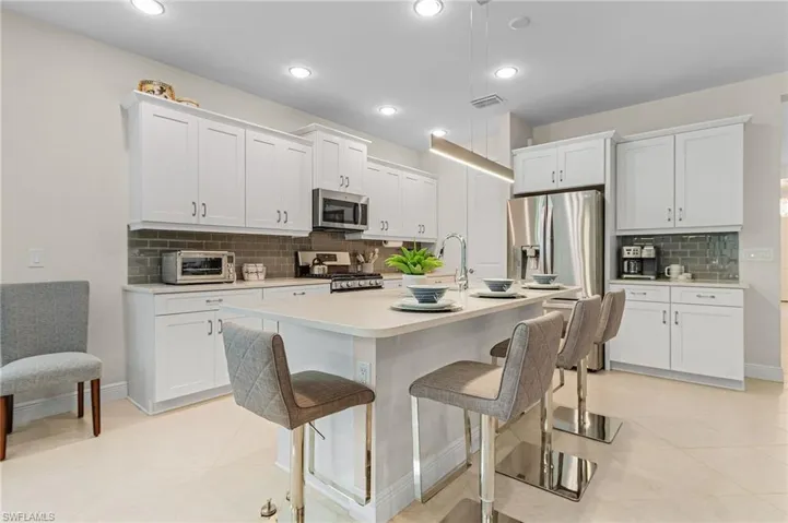 Kitchen featuring light tile flooring, backsplash, white cabinetry, and appliances with stainless steel finishes