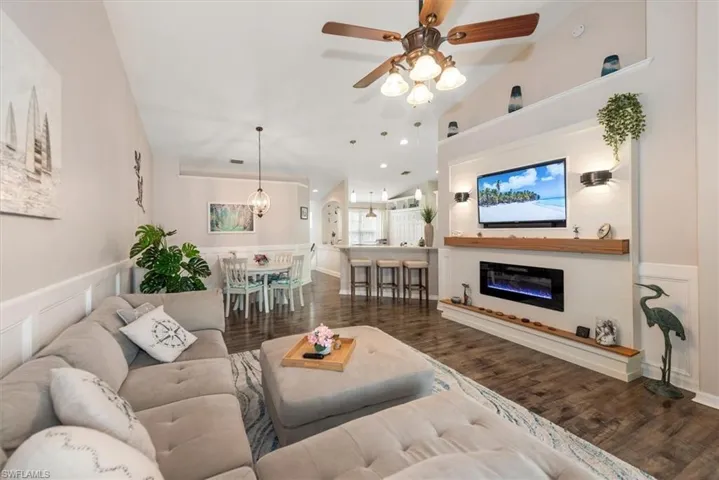 Living area featuring a glass covered fireplace, lofted ceiling, dark wood finished floors, a ceiling fan, and a chandelier