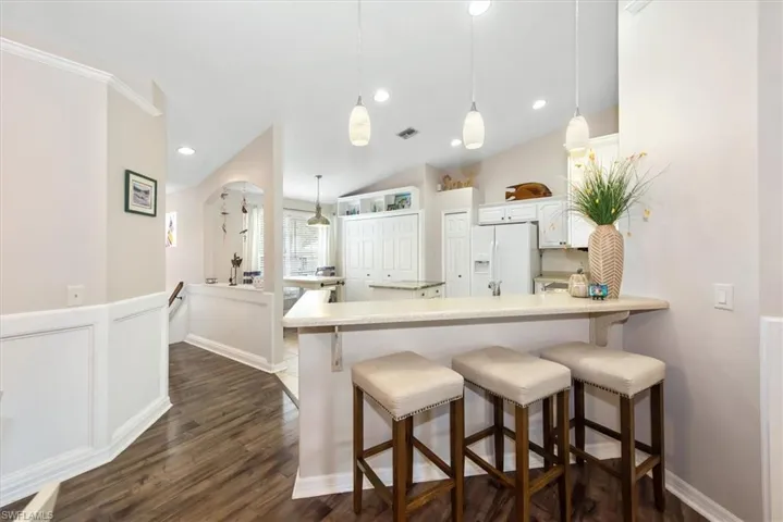 Kitchen with a breakfast bar, a peninsula, hanging light fixtures, white refrigerator with ice dispenser, and recessed lighting