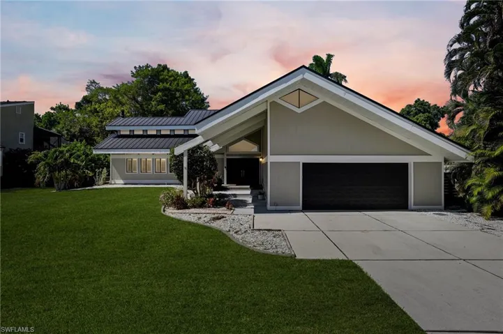 Contemporary architecture featuring a prominent gable roofline, light-toned exterior siding, and a dark garage door