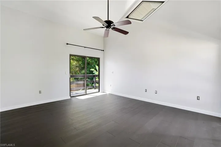 Vaulted ceiling room featuring dark wood-finish flooring, a contemporary ceiling fan, and a skylight