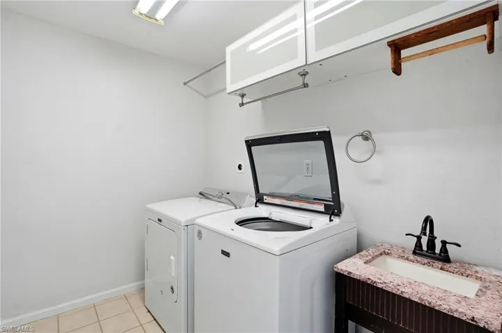 Laundry area featuring a top-load washer, a dryer, and a vanity with a stone-finish countertop