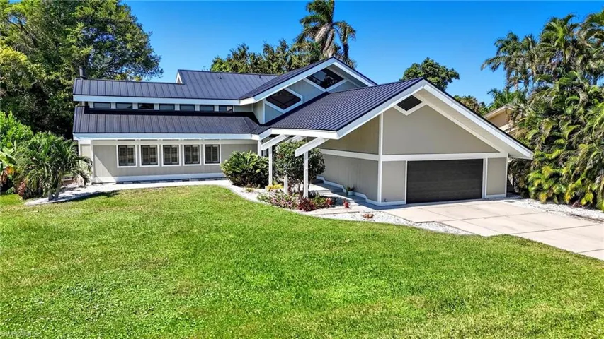 Contemporary residence featuring a dark metal roof, light-toned siding, and a prominent two-car garage with a dark door