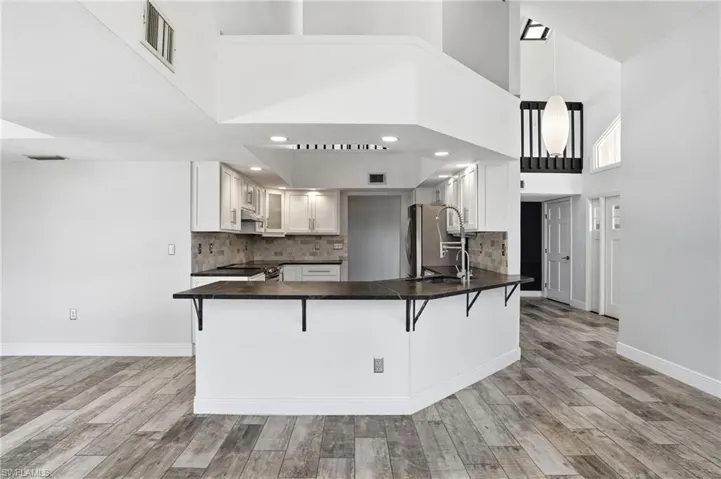 Open-concept kitchen featuring white cabinetry, dark countertops, a tile backsplash, and stainless steel appliances