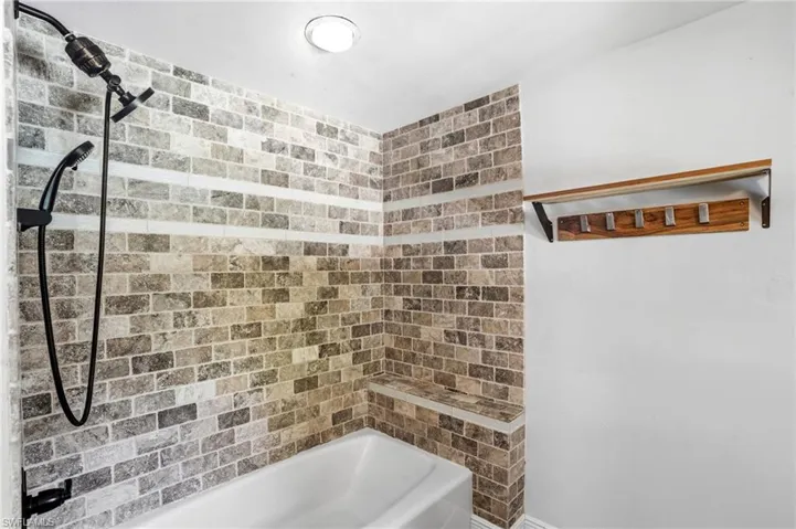 Shower with brick-patterned tile surround, featuring a built-in bench and matte black fixtures