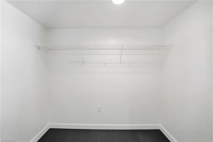 Interior closet space featuring a wire shelving unit, dark wood-finish flooring, white baseboards, and a ceiling-mounted light fixture