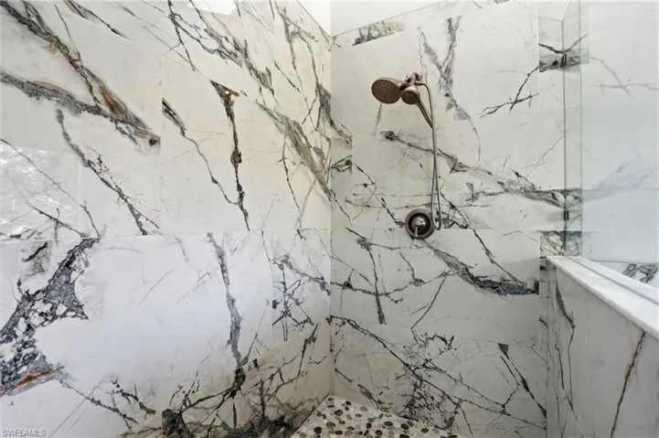 Shower enclosure featuring large format stone-look tile walls, a handheld shower fixture, a built-in shower bench, and a pebble-tile shower floor