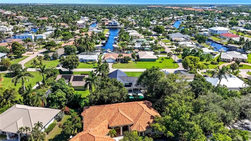 Expansive aerial capturing a vibrant residential area featuring numerous properties with diverse architectural styles, mature trees, and visible waterways with docked boats