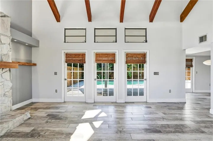 Spacious living area featuring exposed wood ceiling beams, a stone-clad fireplace with a wood mantle, and multiple French doors offering direct outdoor access