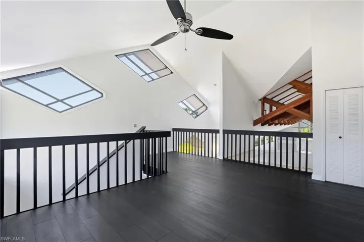 Open loft area featuring dark wood-finish flooring, a sleek black railing, and white vaulted ceilings
