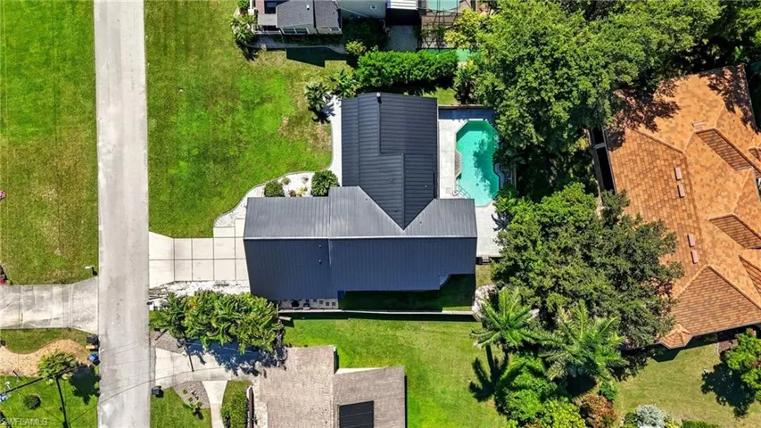 Aerial overview showcasing a property with a dark-pitched roof, a swimming pool, and a concrete driveway