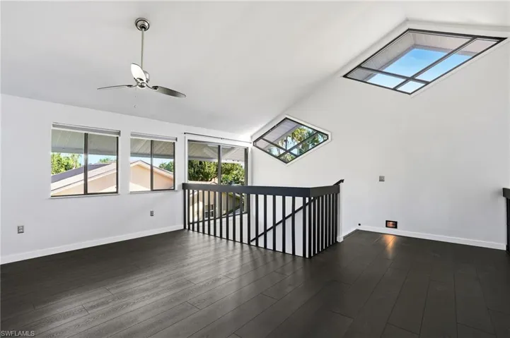 Loft area featuring dark wood-finish flooring, a contemporary ceiling fan, and multiple windows