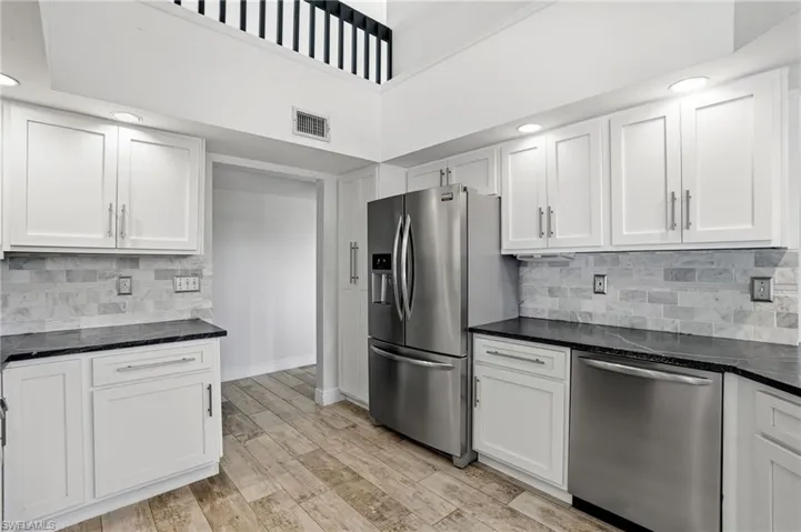 Kitchen featuring white shaker cabinetry, dark countertops, a subway tile backsplash, stainless steel appliances, and wood-finish flooring
