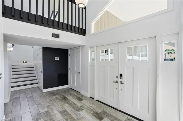 Entryway featuring dual paneled doors with transom windows, wood-finish flooring, a contemporary staircase with integrated lighting, a contrasting accent wall, and a second-story interior balcony with black railings