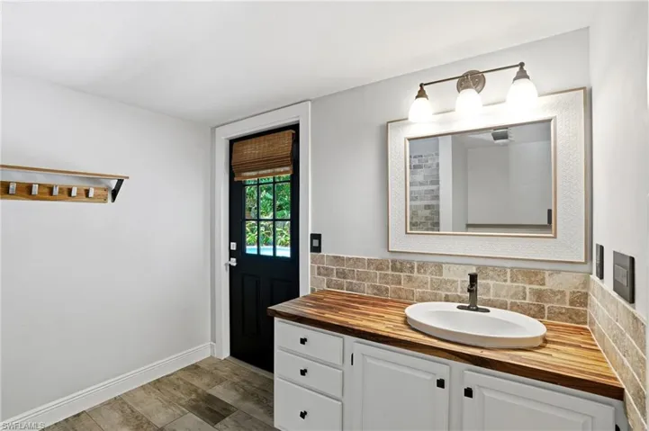 Vanity featuring a vessel sink, wood-finish countertop, and white cabinetry with dark hardware