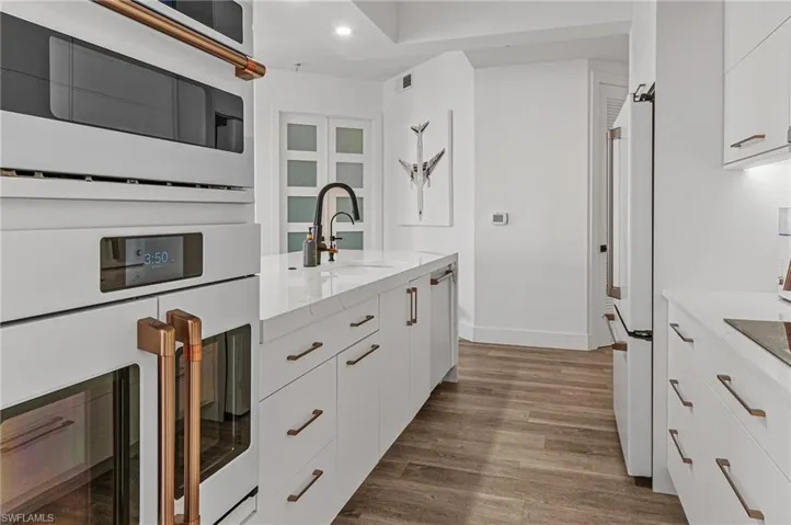 Kitchen with white appliances, light stone countertops, dark wood finished floors, white cabinetry, and a sink