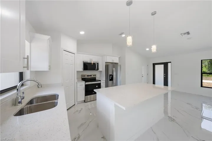 Kitchen featuring visible vents, a sink, appliances with stainless steel finishes, white cabinetry, and vaulted ceiling