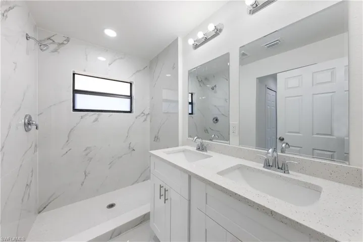 Bathroom featuring double vanity, a marble finish shower, a sink, and visible vents