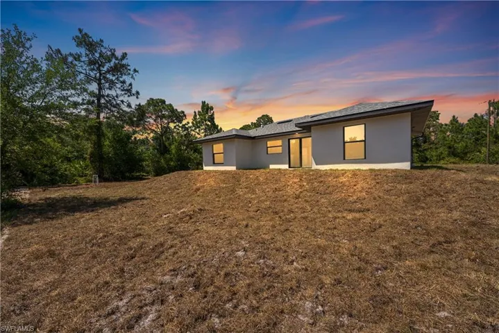 Back of property at dusk featuring stucco siding and a lawn