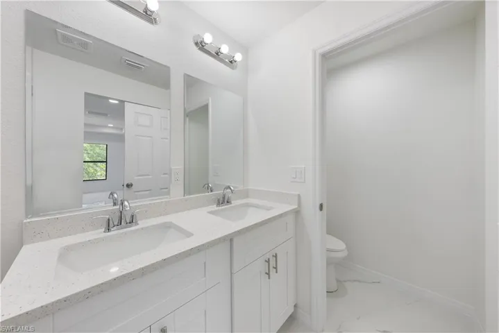 Bathroom with toilet, marble finish floor, a sink, and visible vents