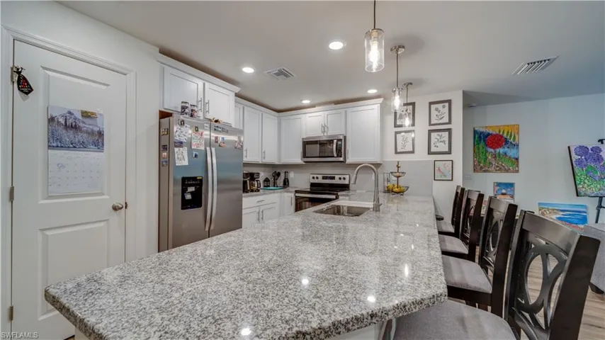 Kitchen with appliances with stainless steel finishes, white cabinetry, a peninsula, a kitchen bar, and light stone counters