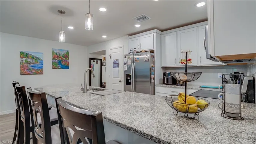 Kitchen featuring light stone counters, stainless steel fridge with ice dispenser, white cabinetry, a kitchen breakfast bar, and pendant lighting