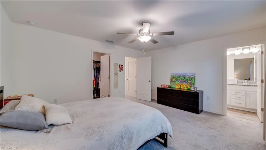 Bedroom featuring a walk in closet, light colored carpet, ensuite bathroom, and ceiling fan