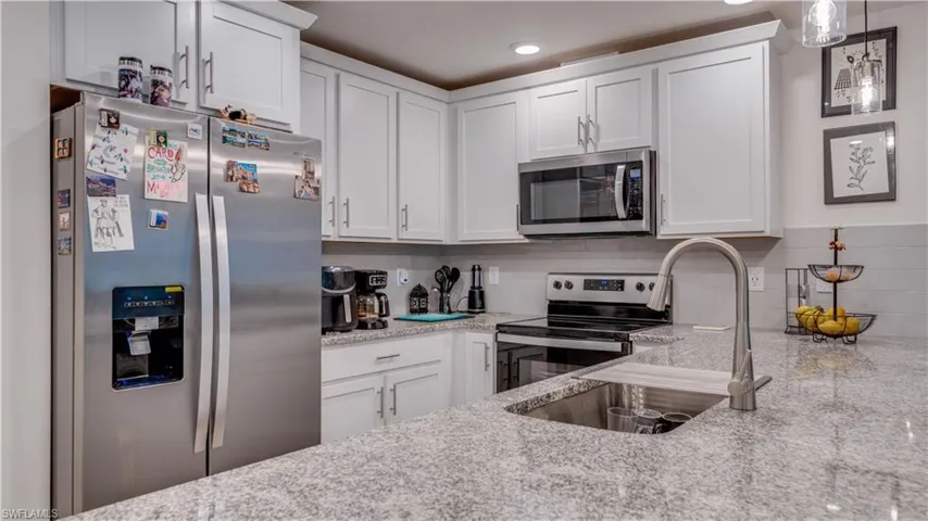 Kitchen featuring appliances with stainless steel finishes, tasteful backsplash, light stone countertops, white cabinetry, and pendant lighting