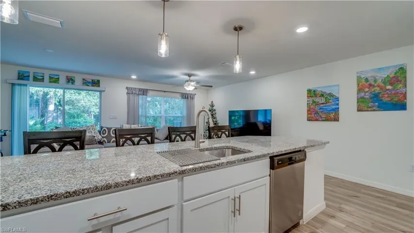 Kitchen with hanging light fixtures, white cabinets, a ceiling fan, stainless steel dishwasher, and light stone counters
