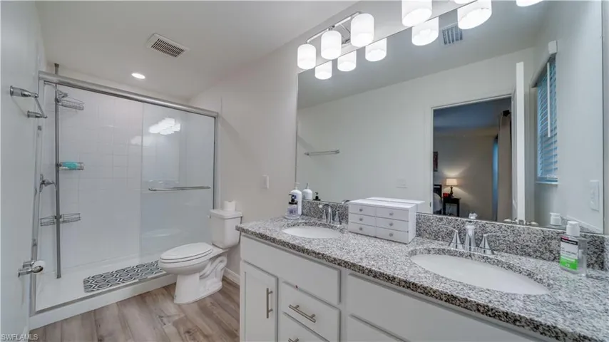 Ensuite bathroom with double vanity, light wood-style floors, a stall shower, and recessed lighting