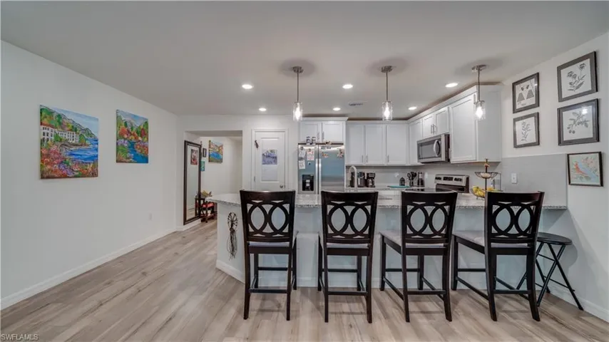 Kitchen with a peninsula, white cabinets, light stone counters, stainless steel appliances, and a kitchen breakfast bar