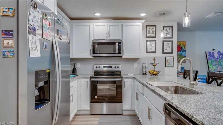 Kitchen featuring appliances with stainless steel finishes, white cabinets, light stone counters, and decorative backsplash