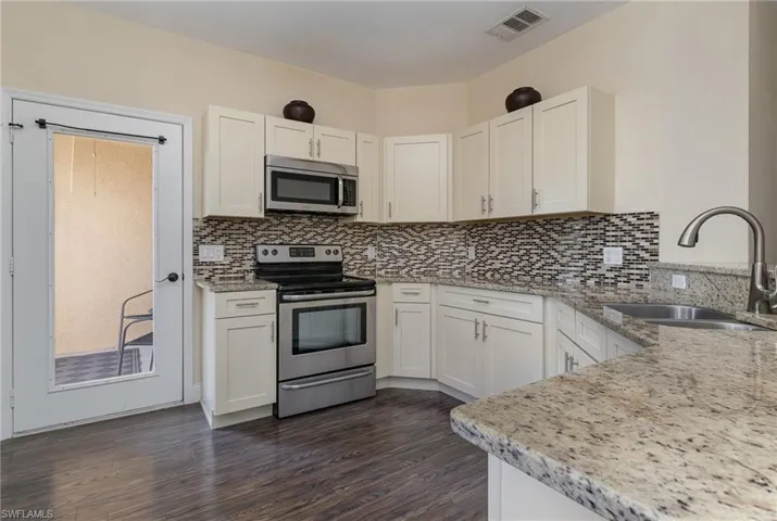 Kitchen featuring sink, appliances with stainless steel finishes, white cabinetry, light stone counters, and decorative backsplash