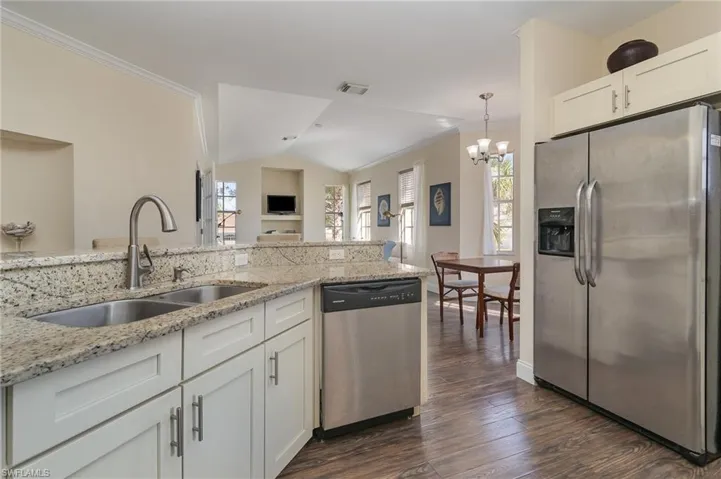 Kitchen with sink, appliances with stainless steel finishes, white cabinetry, hanging light fixtures, and light stone countertops