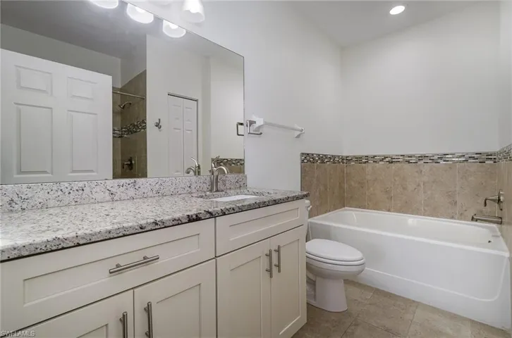 Bathroom with tiled shower, vanity, toilet, and tile patterned flooring