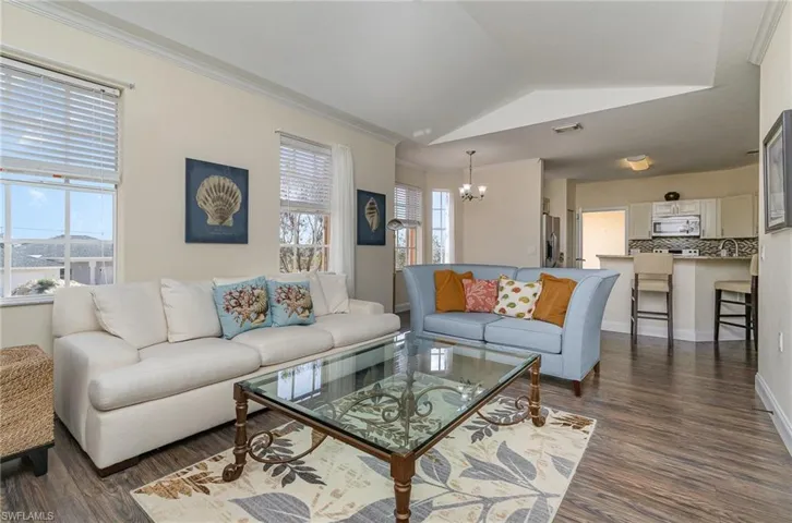 Living room featuring crown molding, an inviting chandelier, vaulted ceiling, and dark wood-type flooring