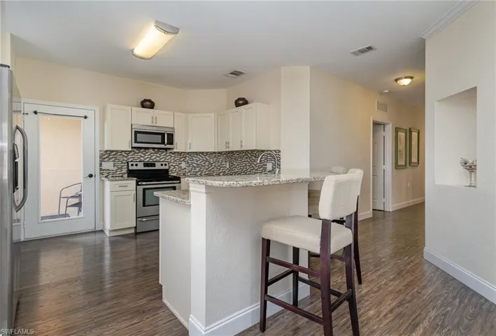 Kitchen with appliances with stainless steel finishes, white cabinetry, a breakfast bar area, light stone counters, and kitchen peninsula